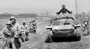 Mai – juin 1940 : C’est la débâcle de l’armée française ! Sous un soleil magnifique, la Wehrmacht déferle sur la France. A droite des soldats français en route vers la captivité qui marchent à contresens de la colonne allemande.